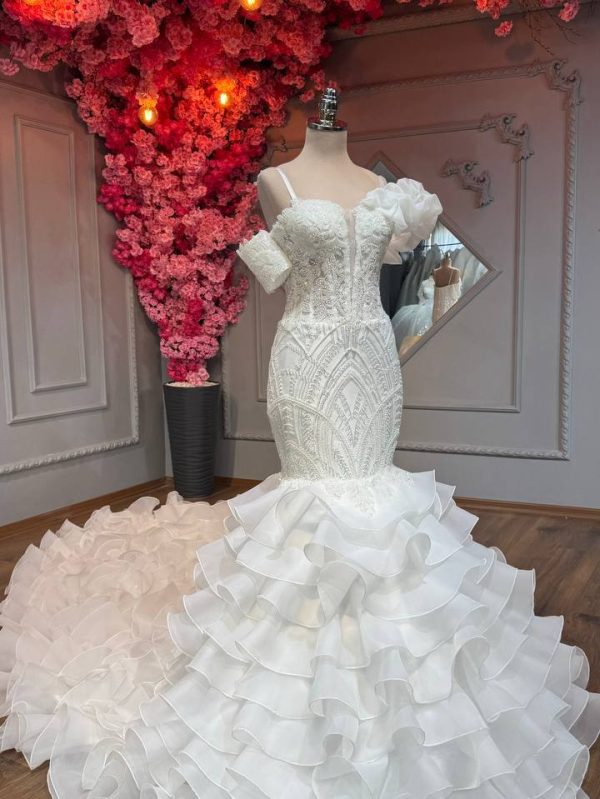 Off-shoulder mermaid wedding dress with beaded bodice and layered ruffle skirt.